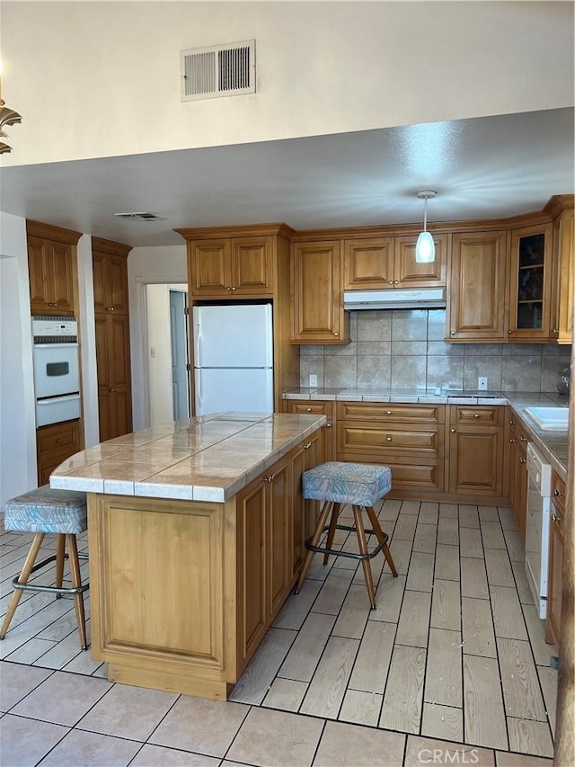 kitchen with a breakfast bar, hanging light fixtures, a kitchen island, white appliances, and backsplash