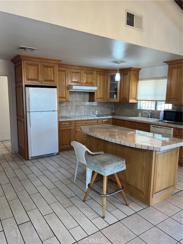 kitchen with a breakfast bar area, tile countertops, a kitchen island, white appliances, and backsplash