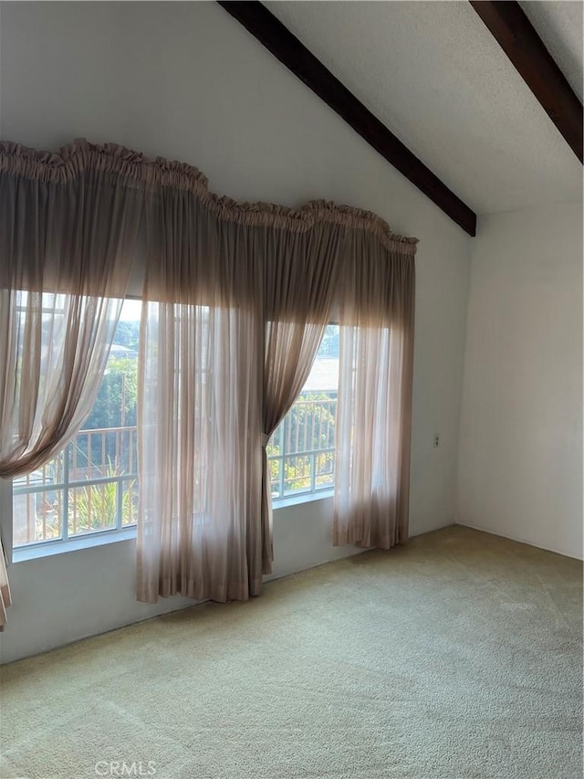 carpeted empty room featuring vaulted ceiling with beams