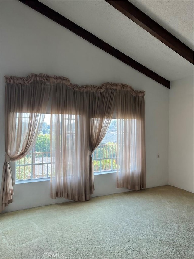 carpeted empty room featuring lofted ceiling with beams and a textured ceiling