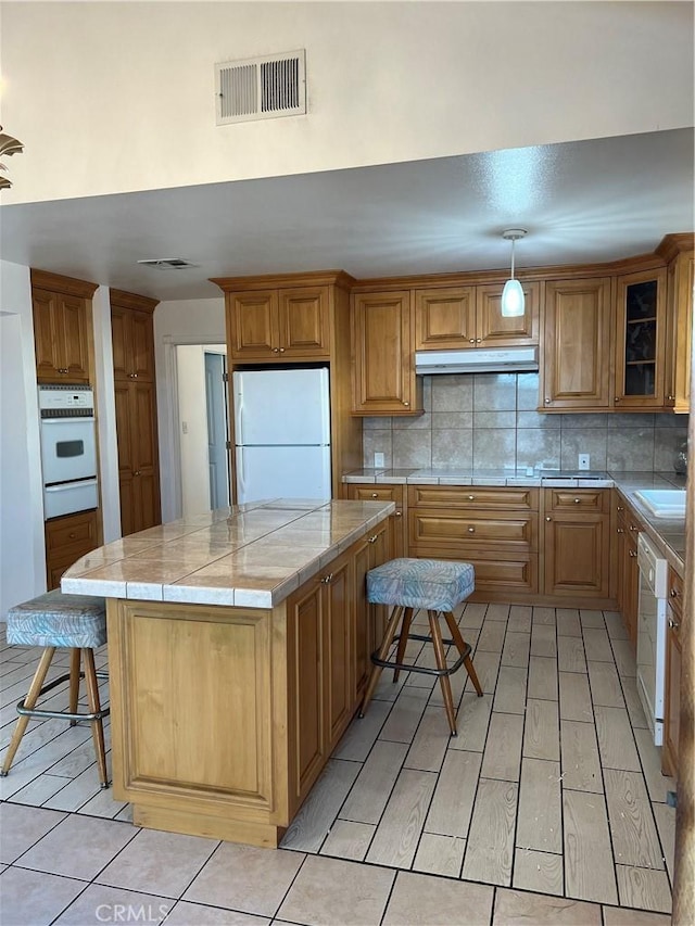 kitchen with white appliances, a kitchen breakfast bar, a center island, tasteful backsplash, and decorative light fixtures