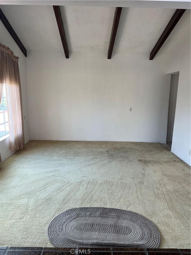 empty room with light carpet, a textured ceiling, and vaulted ceiling with beams