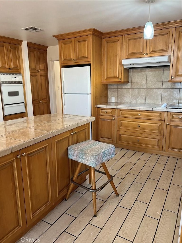 kitchen with backsplash, white appliances, and decorative light fixtures