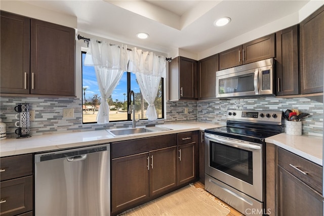 kitchen with sink, light stone countertops, appliances with stainless steel finishes, tasteful backsplash, and dark brown cabinets