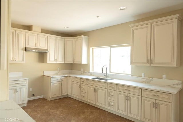 kitchen with light stone counters, sink, and cream cabinetry