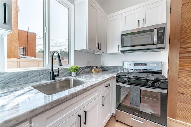 kitchen featuring white cabinetry, sink, light stone counters, and appliances with stainless steel finishes