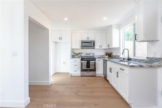 kitchen with appliances with stainless steel finishes, light hardwood / wood-style floors, white cabinetry, and sink