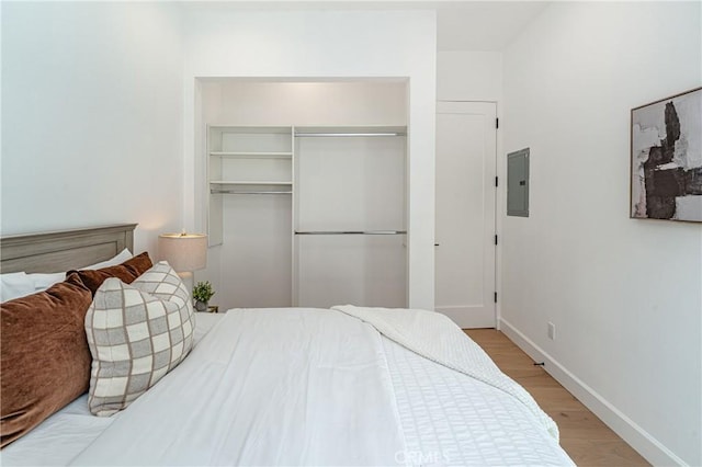 bedroom with light wood-type flooring, electric panel, and a closet