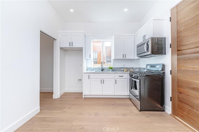 kitchen featuring light stone counters, white cabinets, stainless steel appliances, and light wood-type flooring