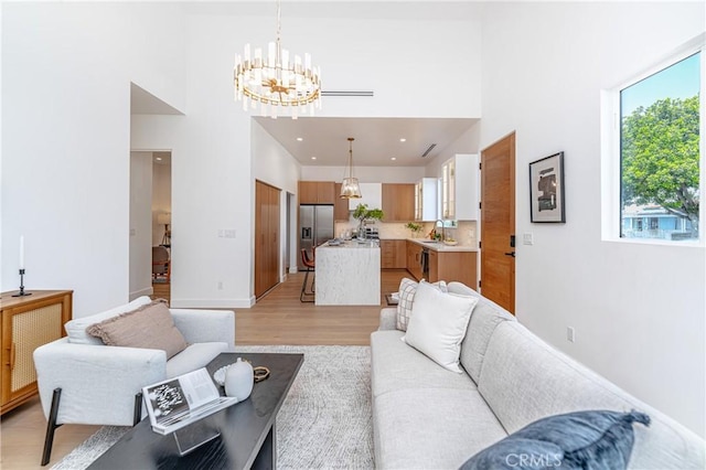 living room with sink, a towering ceiling, light hardwood / wood-style flooring, and an inviting chandelier