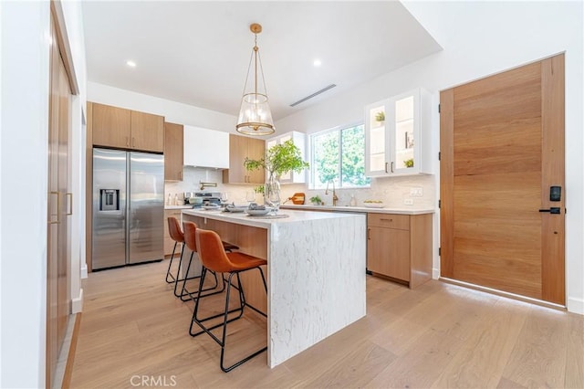 kitchen with decorative backsplash, stainless steel fridge, light wood-type flooring, and a breakfast bar