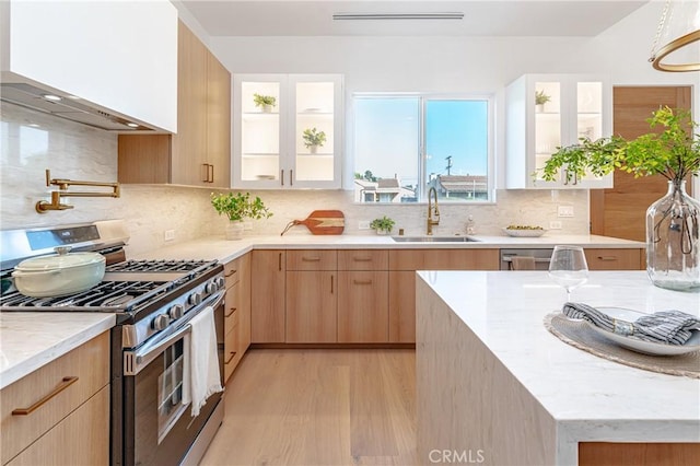 kitchen with decorative backsplash, gas range, sink, light brown cabinets, and light hardwood / wood-style floors