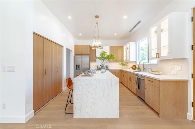 kitchen with sink, hanging light fixtures, light hardwood / wood-style flooring, a kitchen island, and appliances with stainless steel finishes