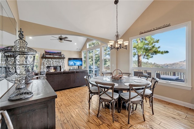 dining room with ceiling fan with notable chandelier, light hardwood / wood-style floors, vaulted ceiling, and a stone fireplace