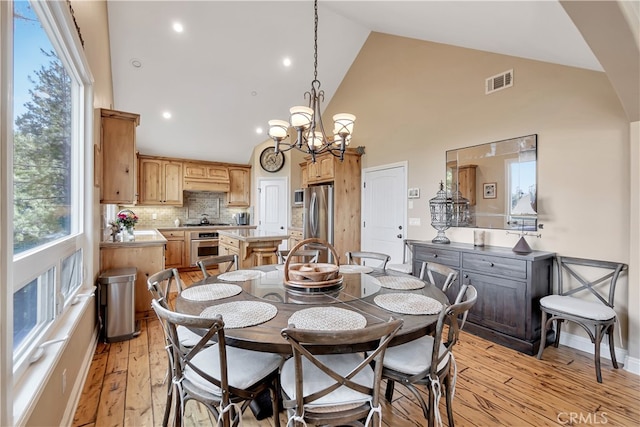 dining room with a notable chandelier, light hardwood / wood-style floors, and high vaulted ceiling