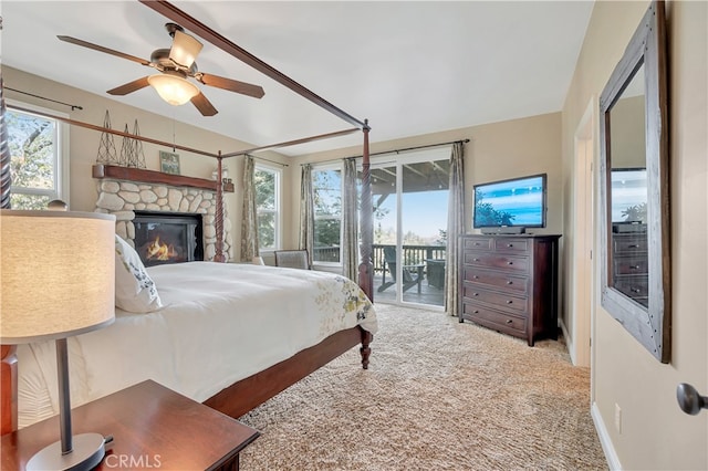 carpeted bedroom featuring access to outside, a stone fireplace, and ceiling fan