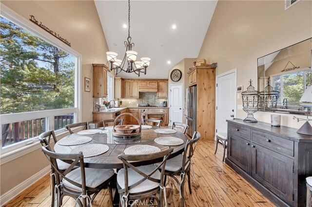 dining room with high vaulted ceiling, a notable chandelier, light wood-type flooring, and sink