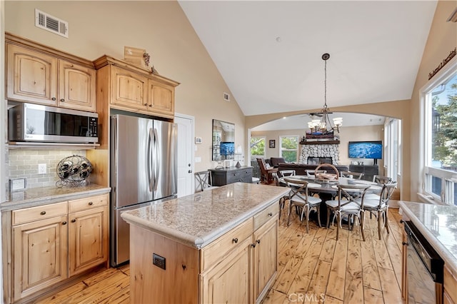 kitchen with appliances with stainless steel finishes, light wood-type flooring, decorative light fixtures, and a center island