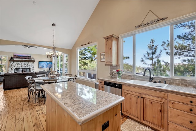 kitchen featuring sink, a kitchen island, a stone fireplace, light wood-type flooring, and a healthy amount of sunlight