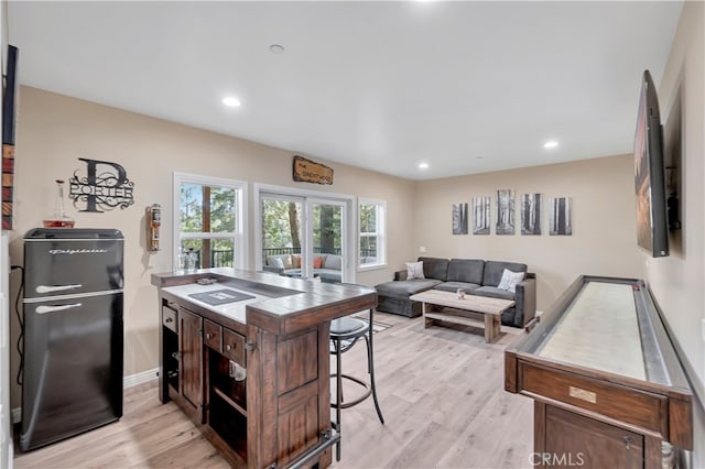 kitchen featuring light hardwood / wood-style floors, dark brown cabinetry, black fridge, a kitchen bar, and a center island