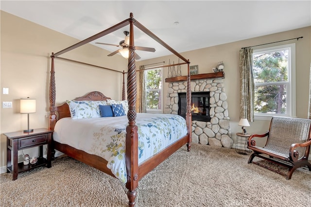 carpeted bedroom featuring ceiling fan and a stone fireplace