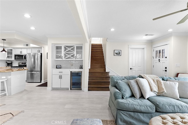 living room featuring ceiling fan, wine cooler, bar area, light wood-type flooring, and crown molding