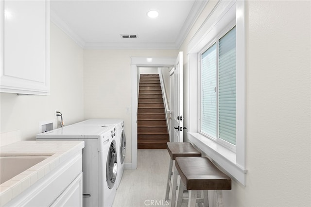 clothes washing area featuring light wood-type flooring, washer and dryer, a wealth of natural light, and cabinets