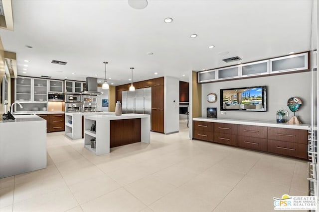 kitchen featuring dark brown cabinetry, a center island, sink, extractor fan, and hanging light fixtures