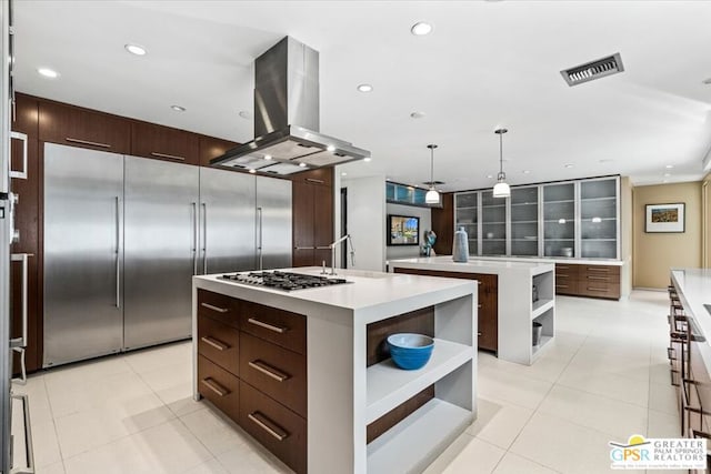 kitchen featuring stainless steel appliances, island range hood, a center island with sink, decorative light fixtures, and light tile patterned floors