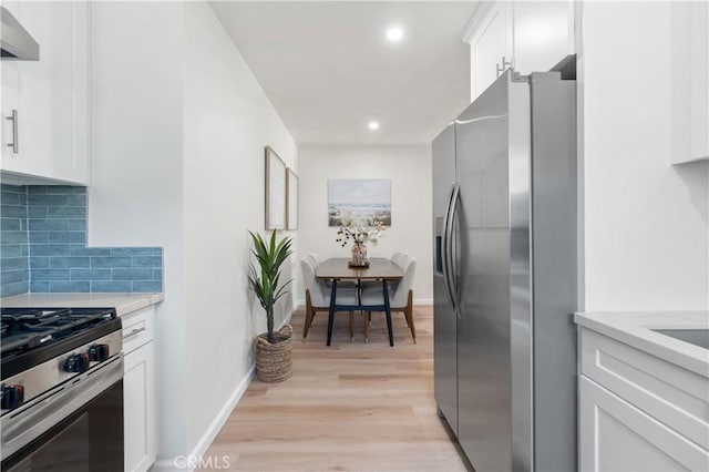 kitchen featuring appliances with stainless steel finishes, light hardwood / wood-style flooring, white cabinetry, and wall chimney exhaust hood