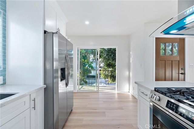 kitchen featuring light hardwood / wood-style flooring, white cabinets, range hood, and appliances with stainless steel finishes