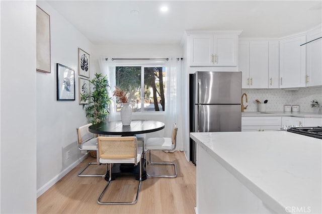 kitchen featuring sink, tasteful backsplash, stainless steel fridge, white cabinets, and light wood-type flooring