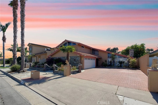 view of front of house featuring decorative driveway, a garage, and fence