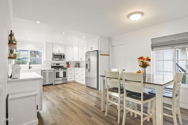 kitchen with white cabinetry, light hardwood / wood-style flooring, stainless steel appliances, and ornamental molding