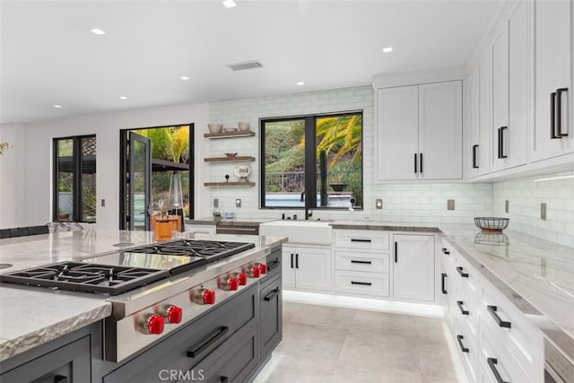 kitchen featuring sink, light stone countertops, tasteful backsplash, white cabinetry, and stainless steel gas cooktop