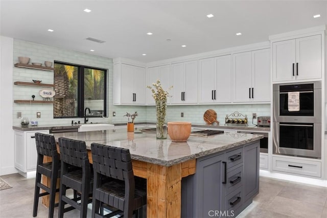 kitchen featuring a kitchen bar, light stone counters, stainless steel double oven, a kitchen island, and white cabinetry