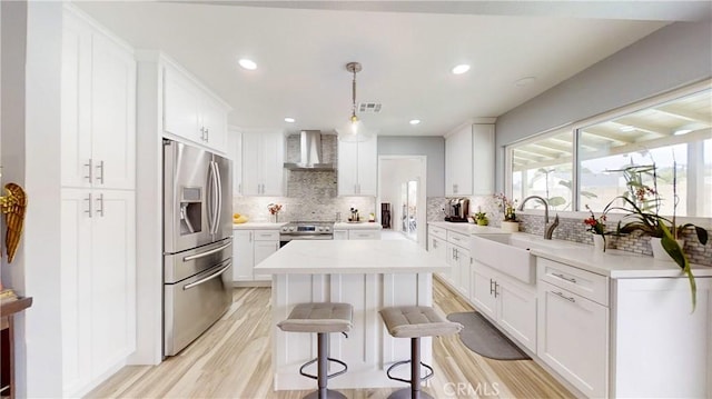 kitchen featuring pendant lighting, white cabinets, wall chimney exhaust hood, light hardwood / wood-style floors, and stainless steel appliances