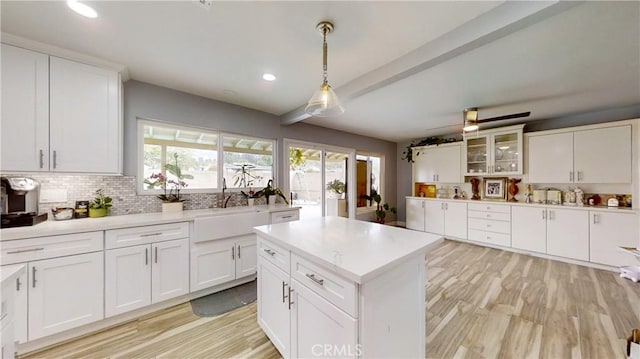 kitchen featuring a kitchen island, tasteful backsplash, decorative light fixtures, white cabinets, and light wood-type flooring