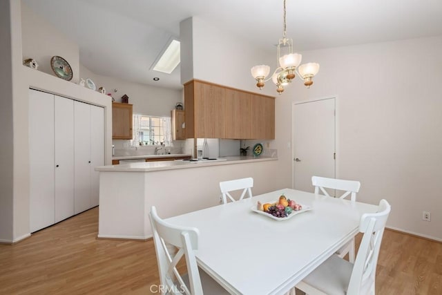 dining area featuring a skylight, sink, light hardwood / wood-style flooring, and an inviting chandelier