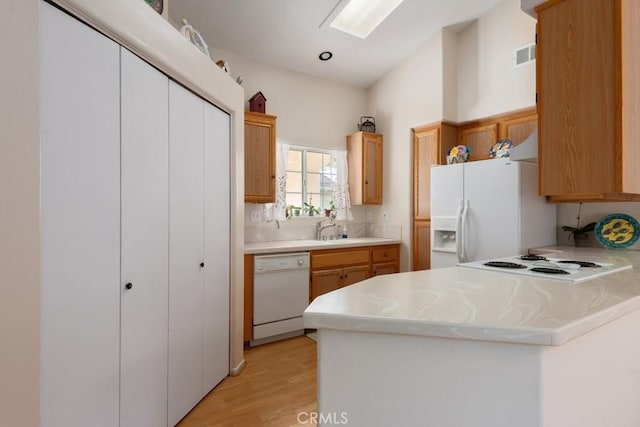 kitchen with light wood-type flooring, white appliances, kitchen peninsula, and sink