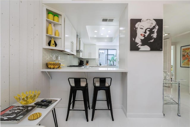 kitchen with white cabinetry, sink, backsplash, kitchen peninsula, and a breakfast bar