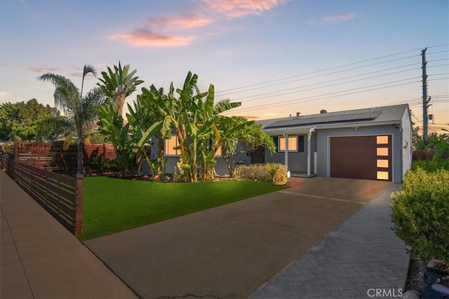 view of front of home featuring a garage, a yard, and solar panels