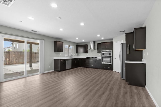 kitchen featuring hardwood / wood-style floors, dark brown cabinetry, wall chimney exhaust hood, stainless steel appliances, and sink