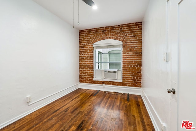 empty room with ceiling fan, cooling unit, dark hardwood / wood-style flooring, and brick wall