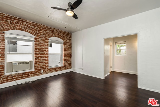 empty room with ceiling fan, cooling unit, dark wood-type flooring, and brick wall