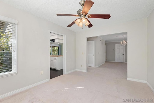 unfurnished room featuring carpet flooring, ceiling fan with notable chandelier, a textured ceiling, and a wealth of natural light