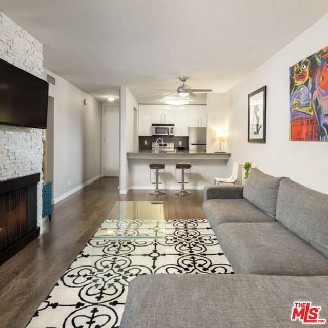 living room with dark wood-type flooring, sink, a fireplace, and ceiling fan