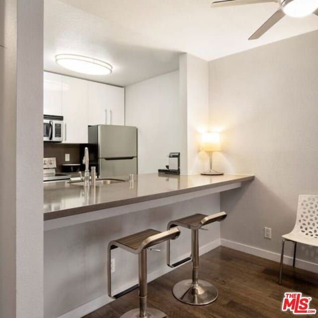 kitchen featuring ceiling fan, white cabinets, appliances with stainless steel finishes, dark hardwood / wood-style floors, and a kitchen bar