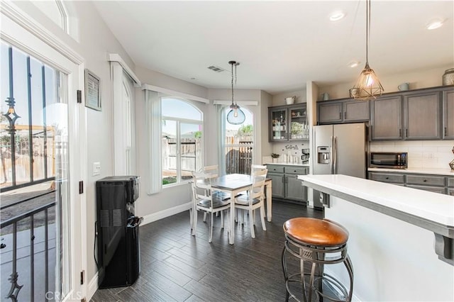 kitchen with dark wood-type flooring, a breakfast bar area, decorative backsplash, decorative light fixtures, and stainless steel appliances