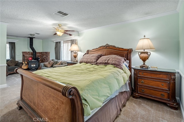 bedroom featuring ceiling fan, light colored carpet, a textured ceiling, and a wood stove